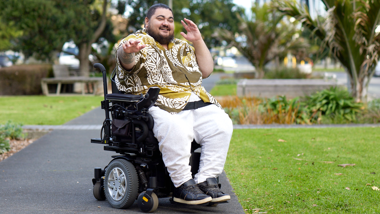 Image of Somaon man sitting in wheelchair, doing dance with his hands, to camera